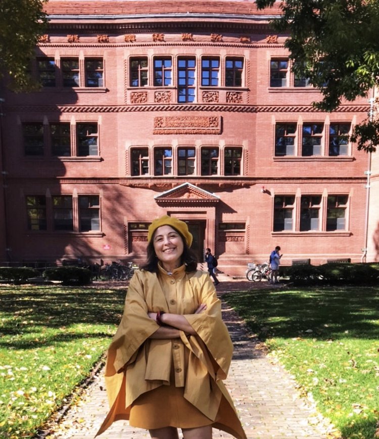 Meryem, sonbahar yapraklarının arasında, Harvard'ın kırmızı tuğlalı binası önünde gülümserken