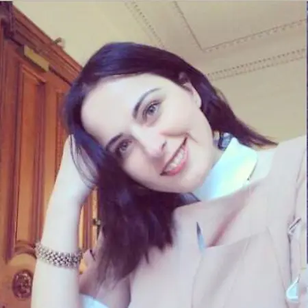 Meryem, sonbahar yapraklarının arasında, Harvard'ın kırmızı tuğlalı binası önünde gülümserken